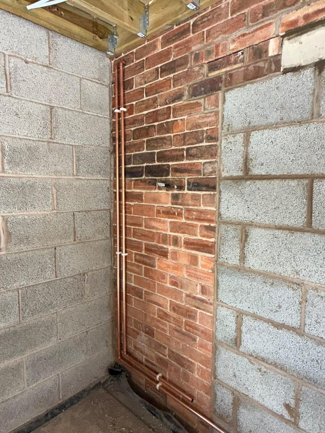 Copper pipe riser clipped up the corner of a brick and block wall in a new extension